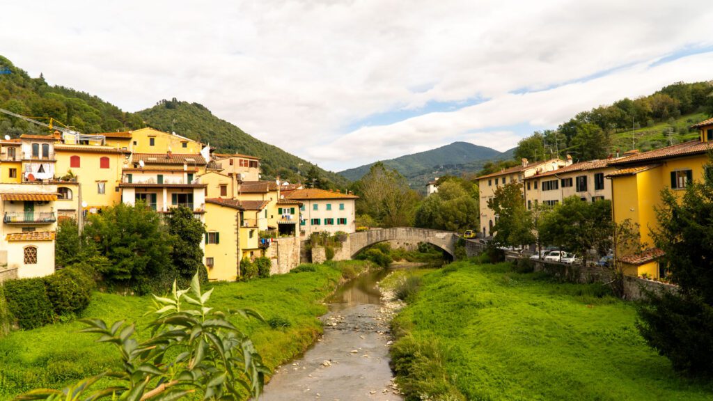 Malerische Ansicht der italienischen Kleinstadt Dicomano mit Fluss, gelben Häusern und einer Steinbrücke vor grünen Hügeln.