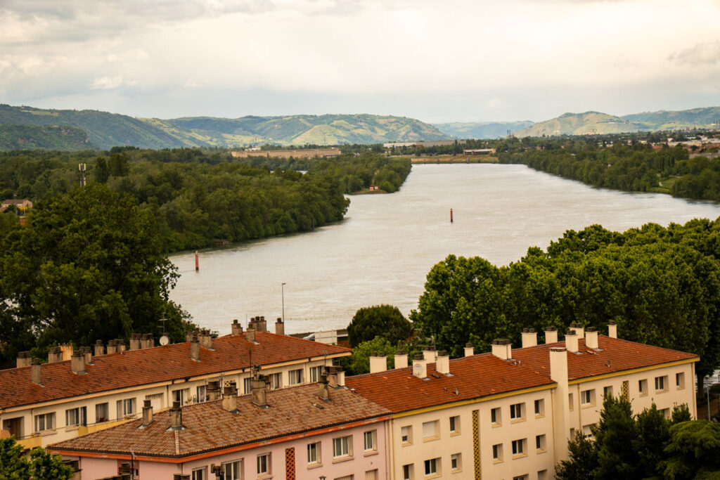 Rio com casas e colinas arborizadas ao fundo